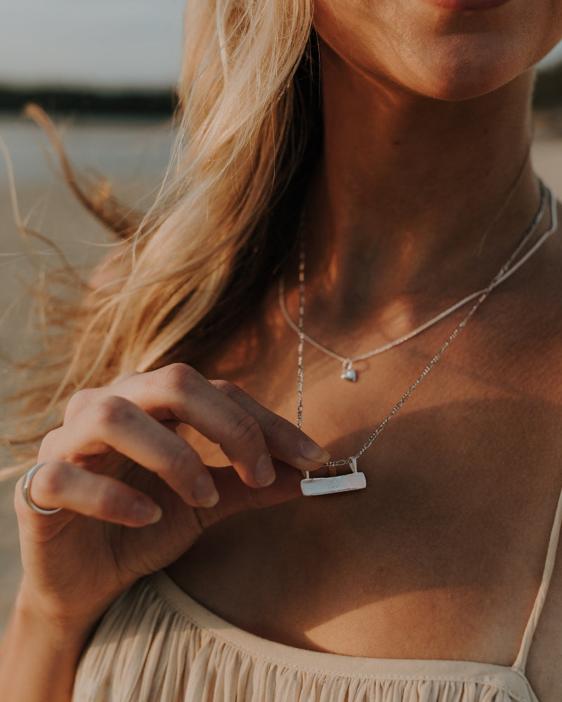 Woman gently holds the Signature Bar Necklace Silver, engraved with a name. A personalised sterling silver gift with heirloom appeal.