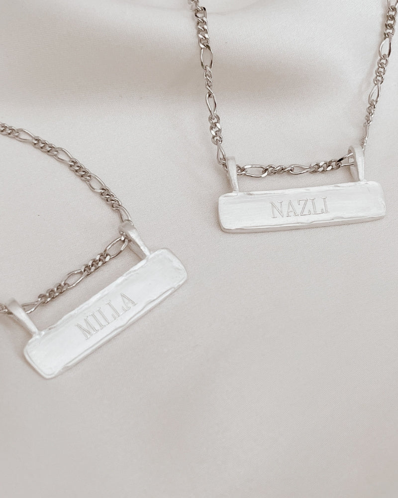 Signature Bar Necklace Silver shown in a flat lay, engraved with “MILLA” and “NAZLI”. A beautiful silver necklace gift for two.