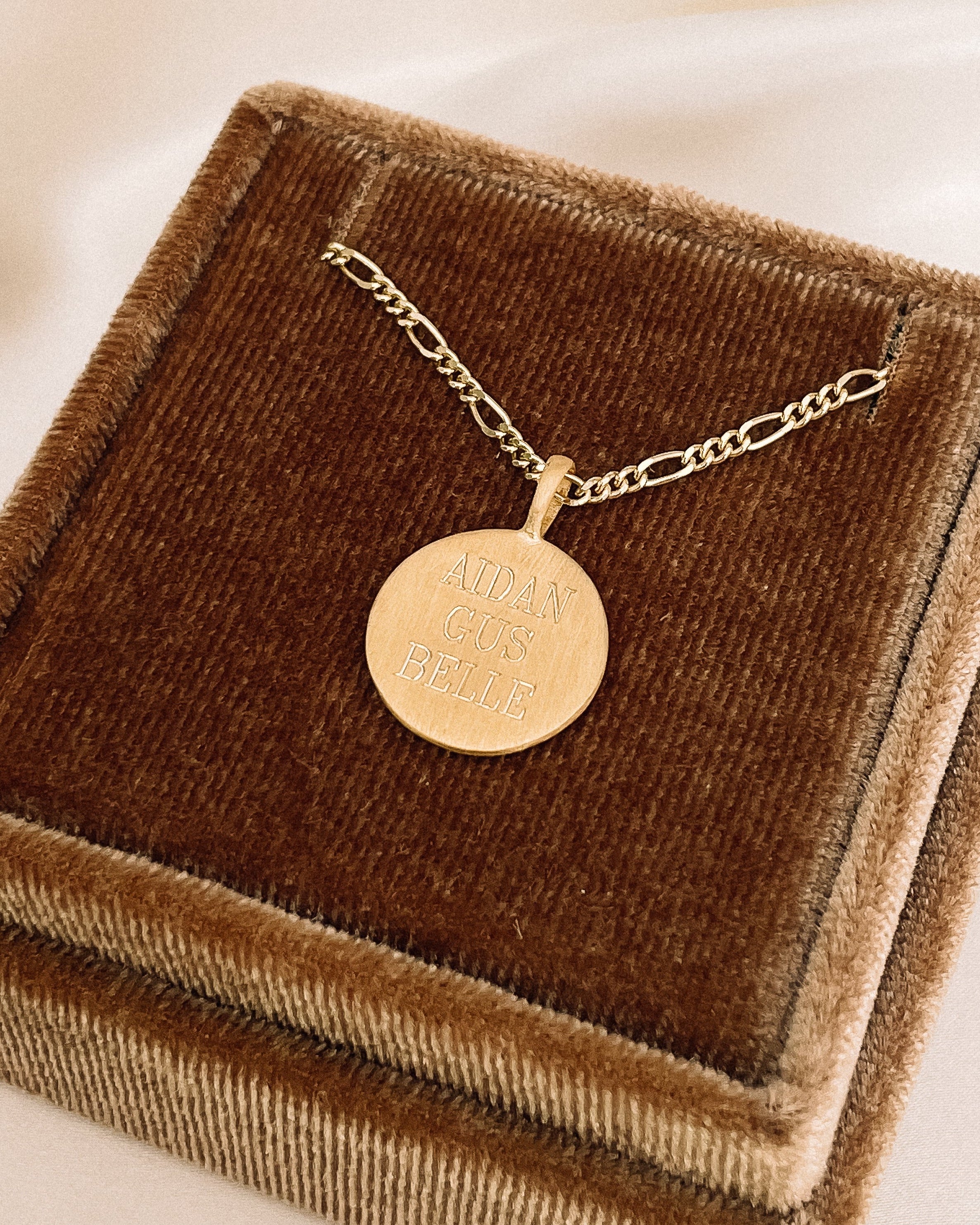 A Signature Necklace with personalised names of three children engraved on the front of it is placed inside a velvet gift box.