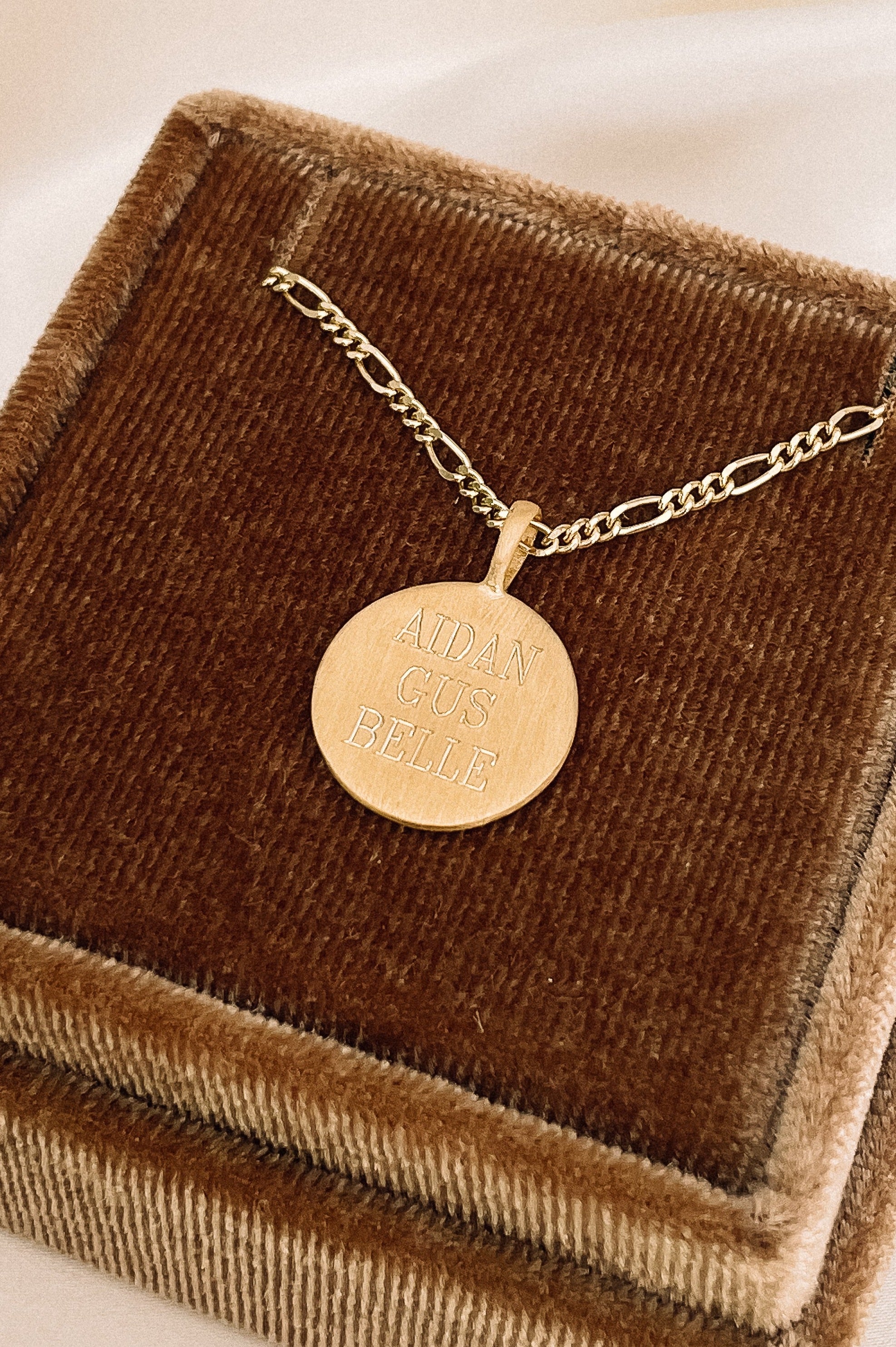 A Signature Necklace with personalised names of three children engraved on the front of it is placed inside a velvet gift box.