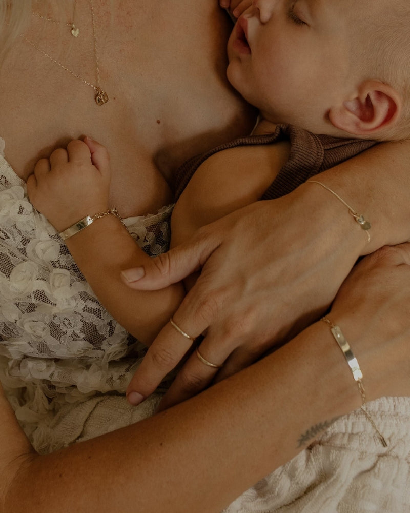 Sleeping baby and mum wearing matching solid gold Darling Bracelets with engraved keepsake plates by Bluebird Jewellery
