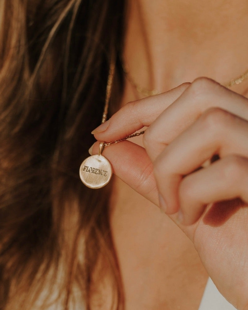 A Signature Necklace with Florence engraved on the front of the pendant is held out by the wearer to show the beautiful detailing on the pendant.