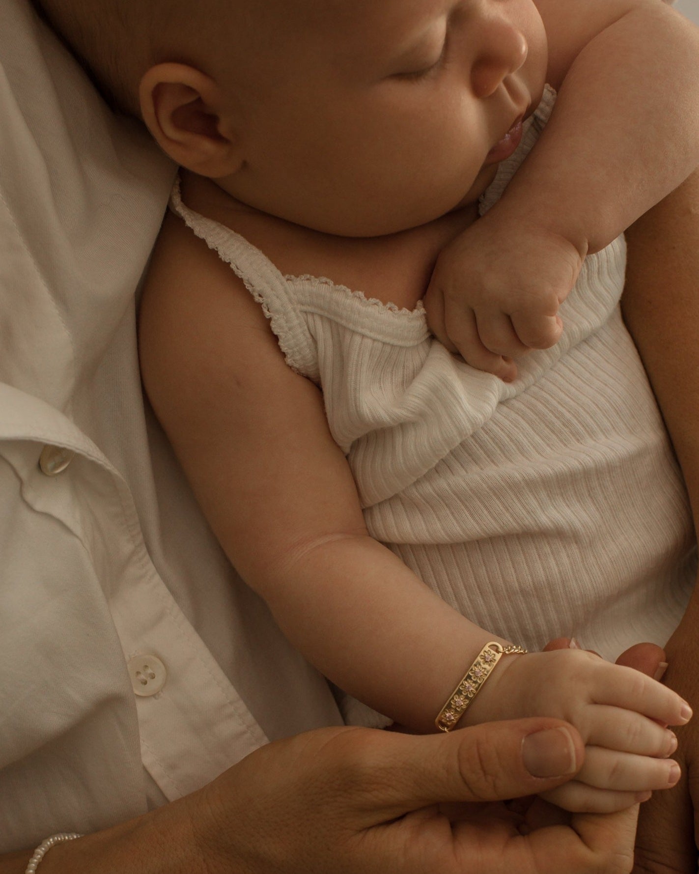 A baby girl is wearing the Daisy Bracelet in Gold Vermeil by Bluebird Jewellery.