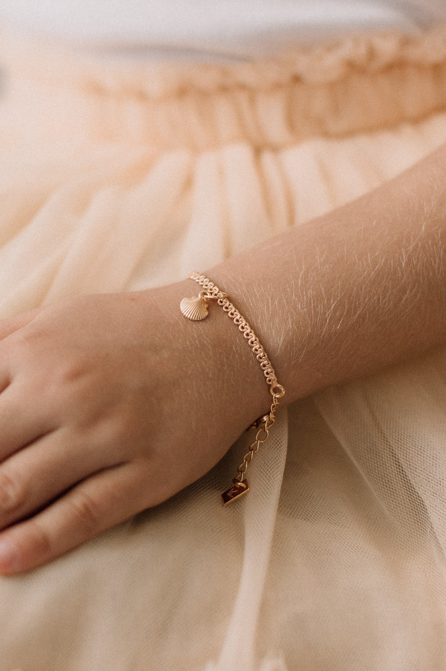 A child wearing a delicate gold Lace Chain bracelet featuring a mermaid shell charm, crafted as a timeless keepsake by Bluebird Jewellery