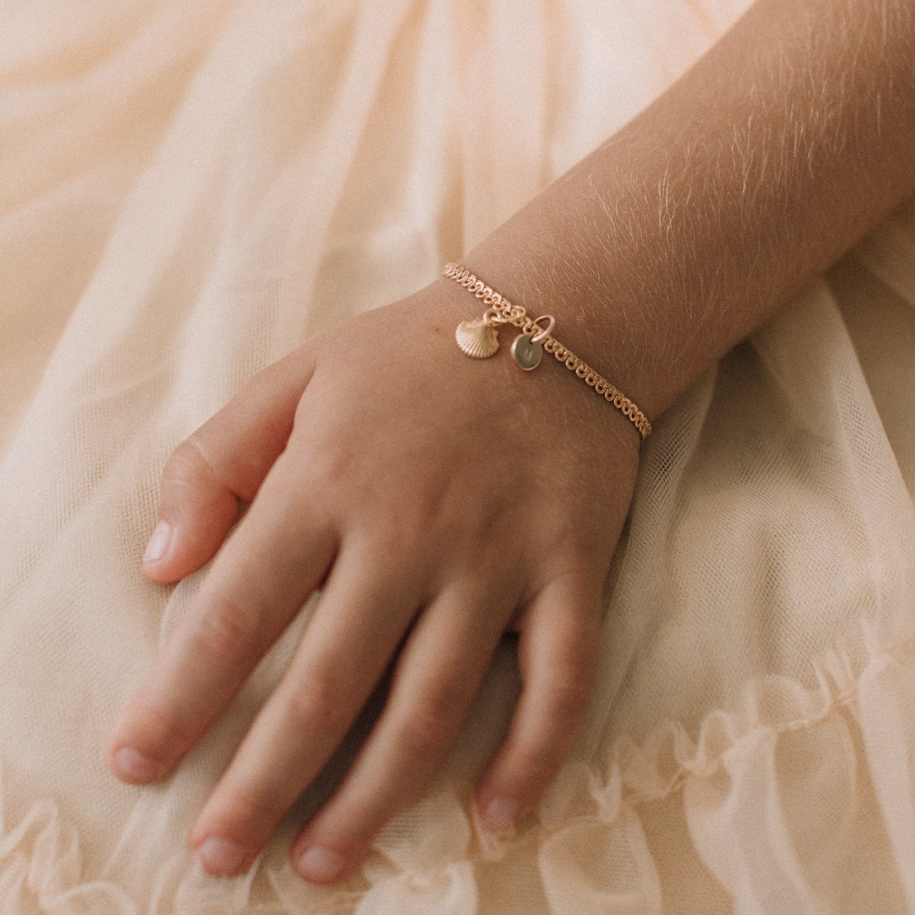 A close-up of a child’s wrist adorned with a gold Lace Chain Anklet with a mermaid shell and soild gold initial pendant, designed as fine personalised jewellery by Bluebird Co
