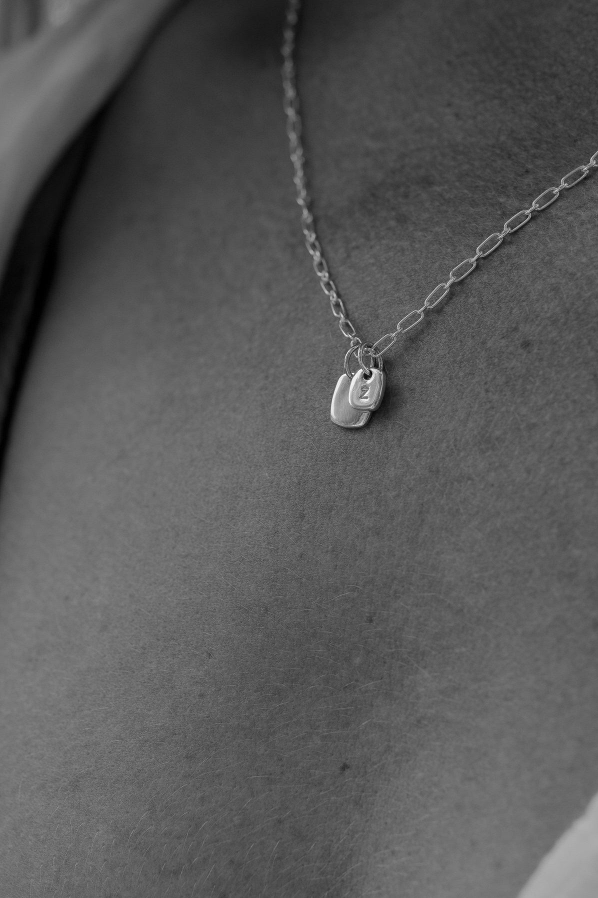 A close up image of a Rectangular Pendant necklace with a regular and mini sized solid sterling silver rectangular pendant rests upon a woman's neck. The mini rectangular pendant is hand stamped with the woman's initial.