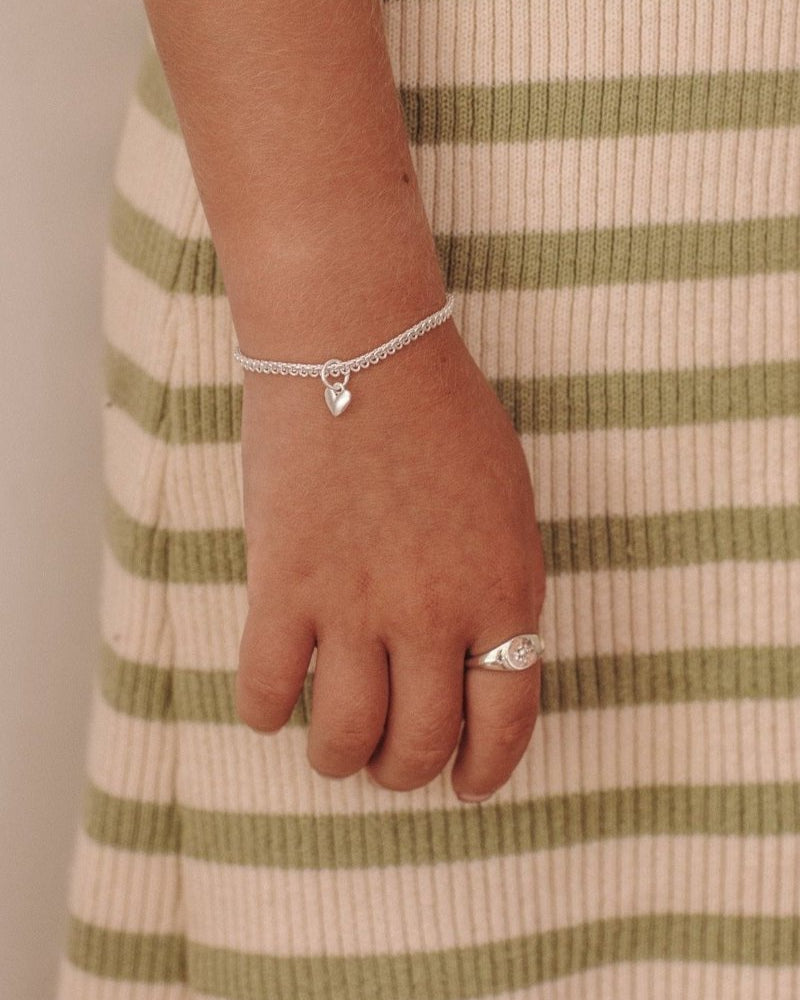 A detailed close-up of a young girl's wrist wearing a gold silver Sweetheart Lace Chain and signet ring, crafted as elegant fine jewellery pieces by Bluebird Co