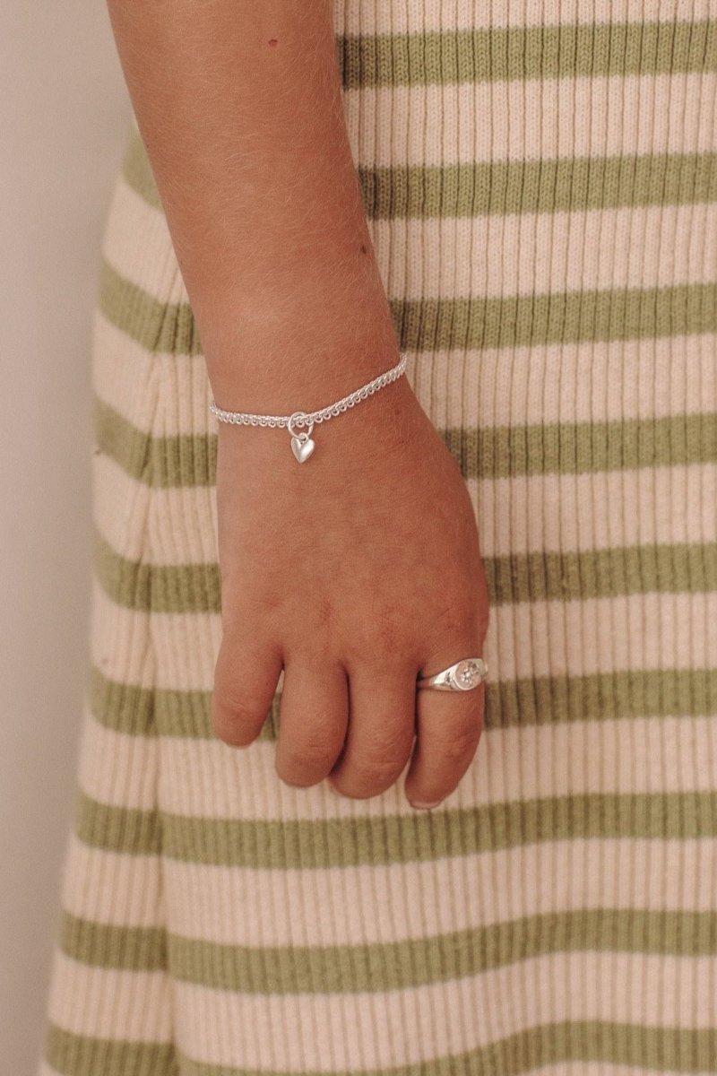 A detailed close-up of a young girl's wrist wearing a gold silver Sweetheart Lace Chain and signet ring, crafted as elegant fine jewellery pieces.