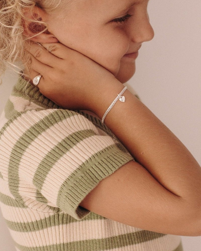 A detailed close-up of a young girl wearing a gold silver Sweetheart Lace Chain and signet ring, crafted as elegant fine jewellery pieces by Bluebird Co