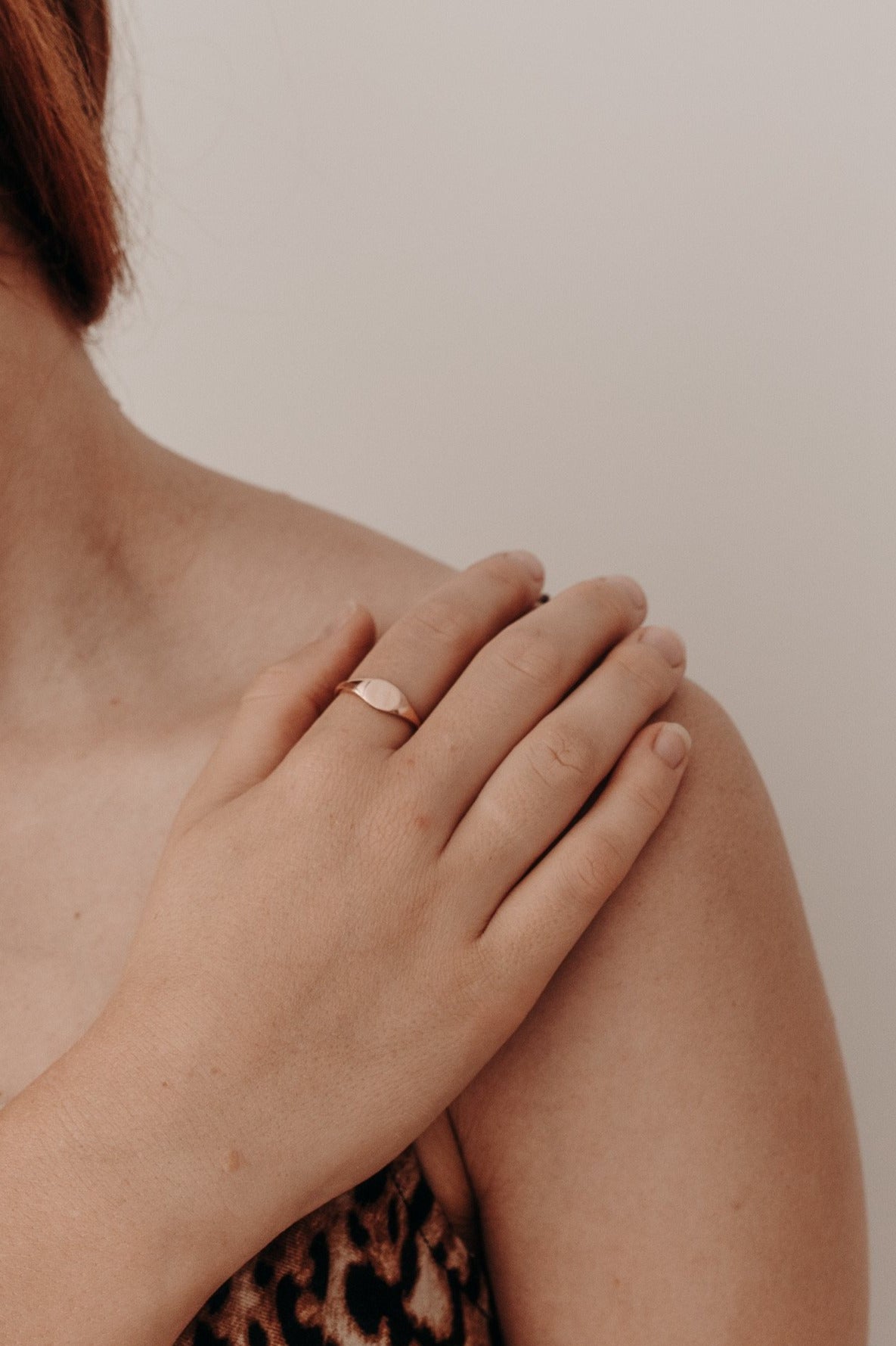 A woman's hand rests elegantly on her shoulder.  The woman is wearing a solid 9ct rose gold signet ring.