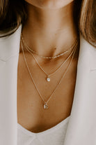 A woman is wearing three necklaces layered and the longest necklace is a Ball Chain Necklace with two Mini Rectangular Initial Pendants in it.