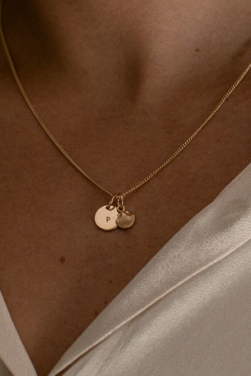 A Keeping it Personal necklace is worn with a mini shell pendant added to it. 