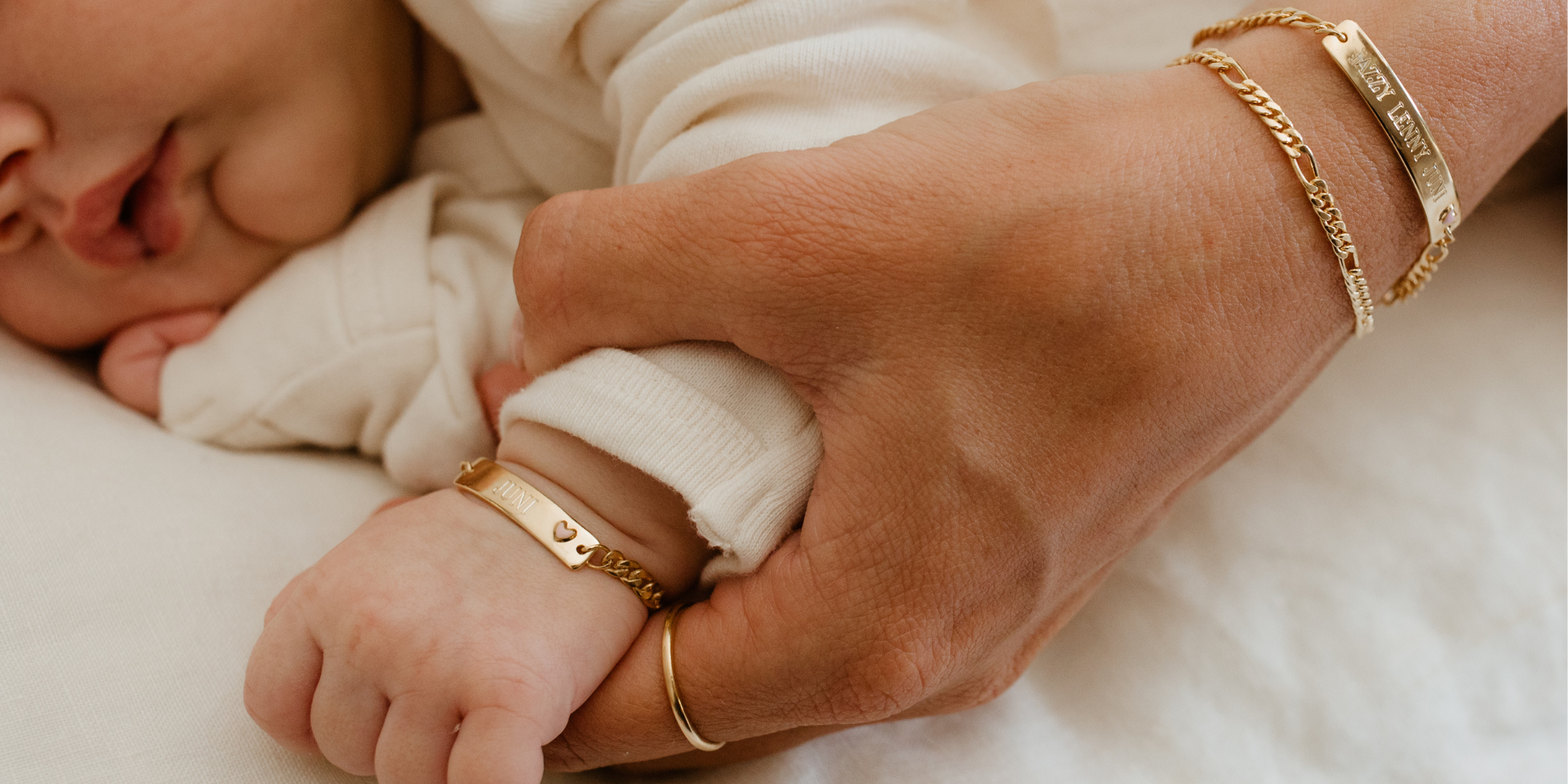 Baby's hand held by an adult hand with gold bracelets on a soft surface