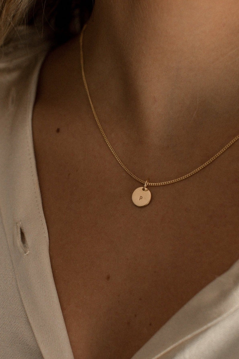 A fine curb chain in gold vermeil rests elegantly on a woman’s neckline and has one initial pendant on it.