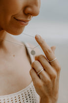 A mother is wearing a Petite Signature Necklace that features a personalised letter engraved on the front of the pendant.