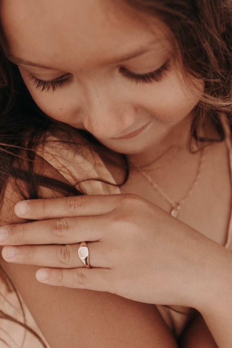 A young girl is looking at her Bluebird Co Jewellery solid 9ct Rose Gold Signet Ring.  it is able to be persoanlised with a machine engraved initial pendant on the front of the ring.