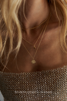 Close-up of a model wearing layered gold necklaces, including a flat circular disc pendant necklace and a delicate chain necklace, paired with a textured metallic top.