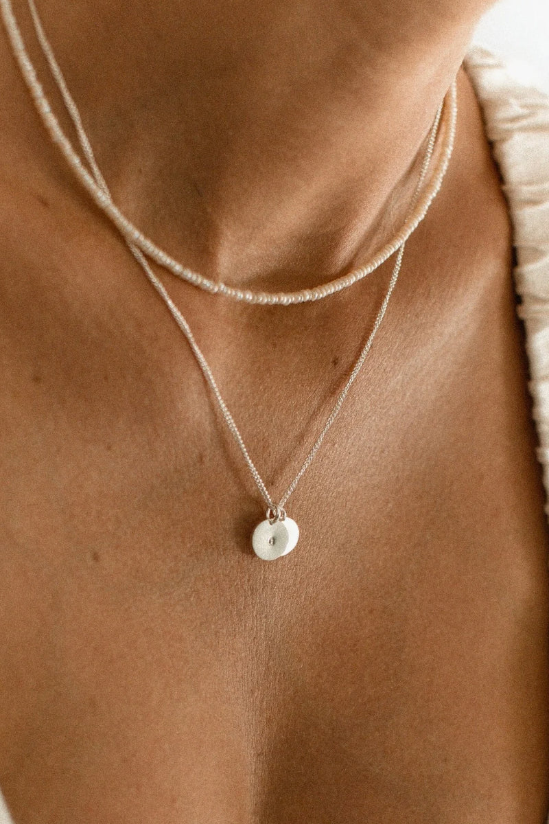 A woman wears a Freshwater Pearl necklace layered with a Keeping it Personal necklace with personalised initial pendants.