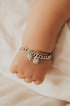 The sweetest close up of a baby wearing a Sweetheart Cuban Link bracelet that has a mini sweetheart pendant on it as well as a mini rectangular initial pendant.