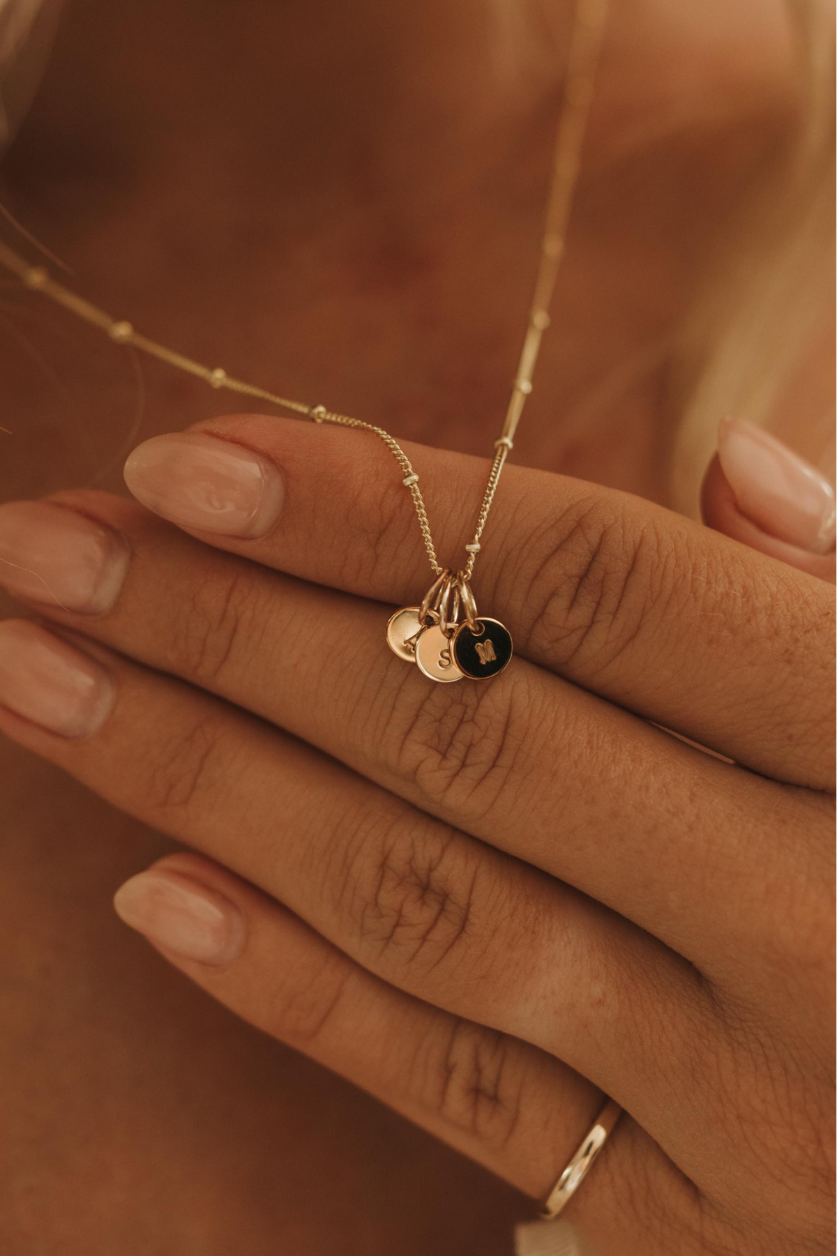 Close-up of a person wearing a delicate necklace with solid gold initial pendants and a heart pendant.