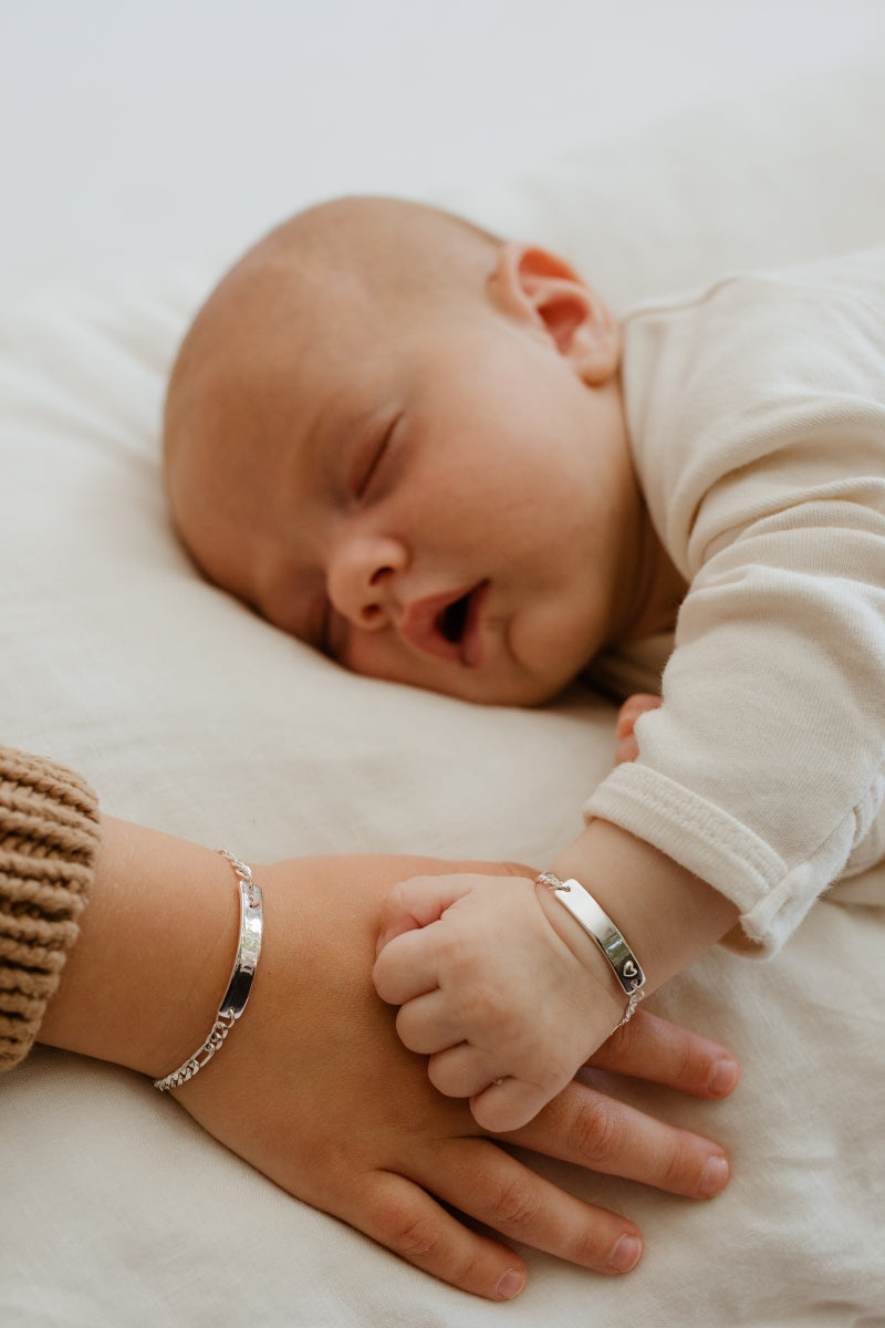 A baby's hand rests on a child's hand.  The baby is wearing a baby sized Darling Bracelet in sterling silver and the child wears the Pink Darling Bracelet .