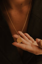 A close up of engraving on a matte finish pendant.  A woman's name is engraved on the front surface of the pendant and she is holding out the chain to show the detailed machine engraving on her personalised pendant.