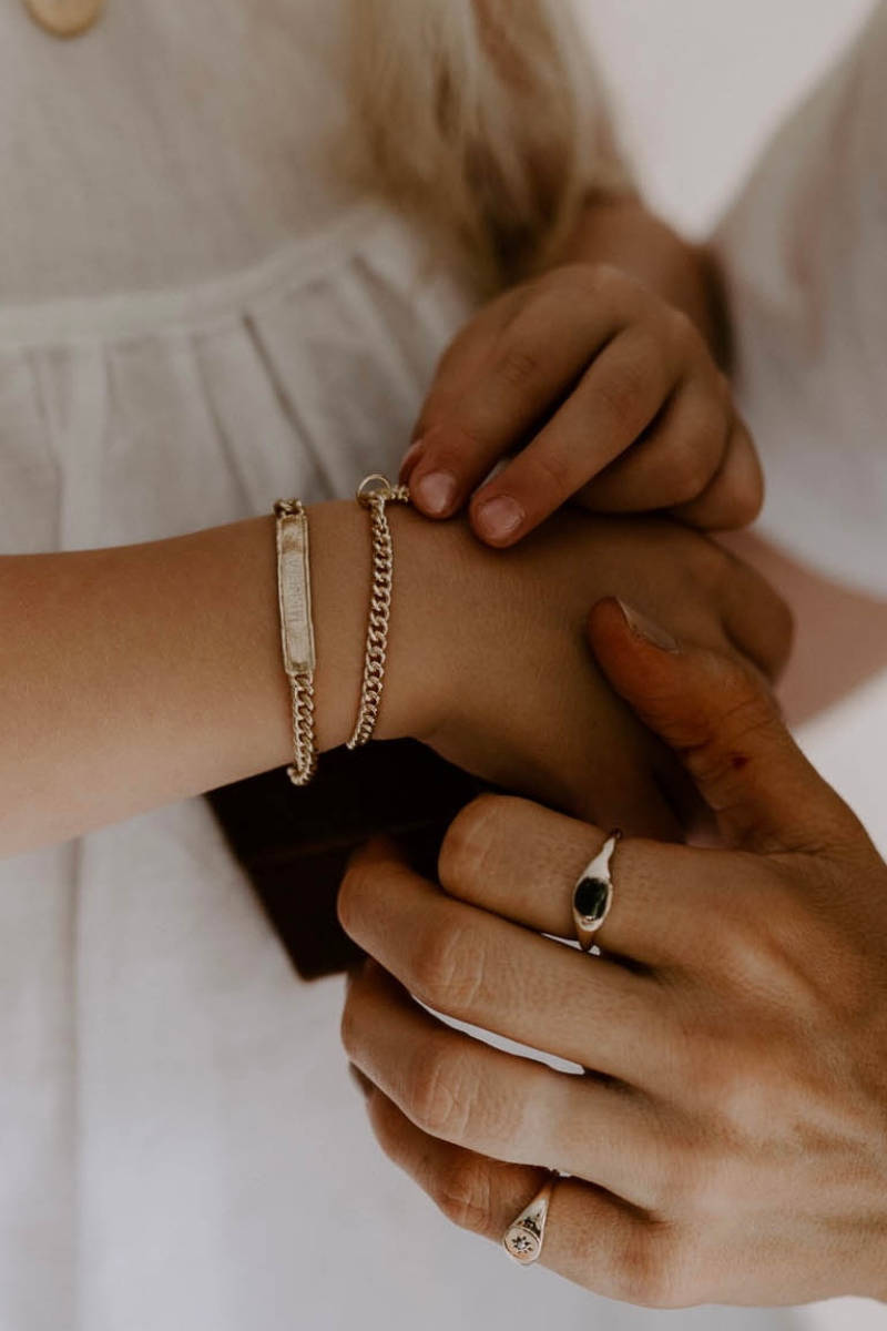 A woman and child wearing personalised gold bracelets and signet rings styled together for an elegant everyday look by Bluebird Jewellery