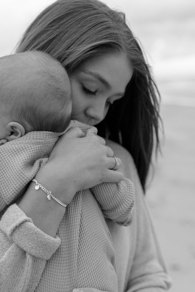 A mum hugging her child, wearing a personalised silver bracelet with engraved initials, designed to celebrate love and family by Bluebird Jewellery