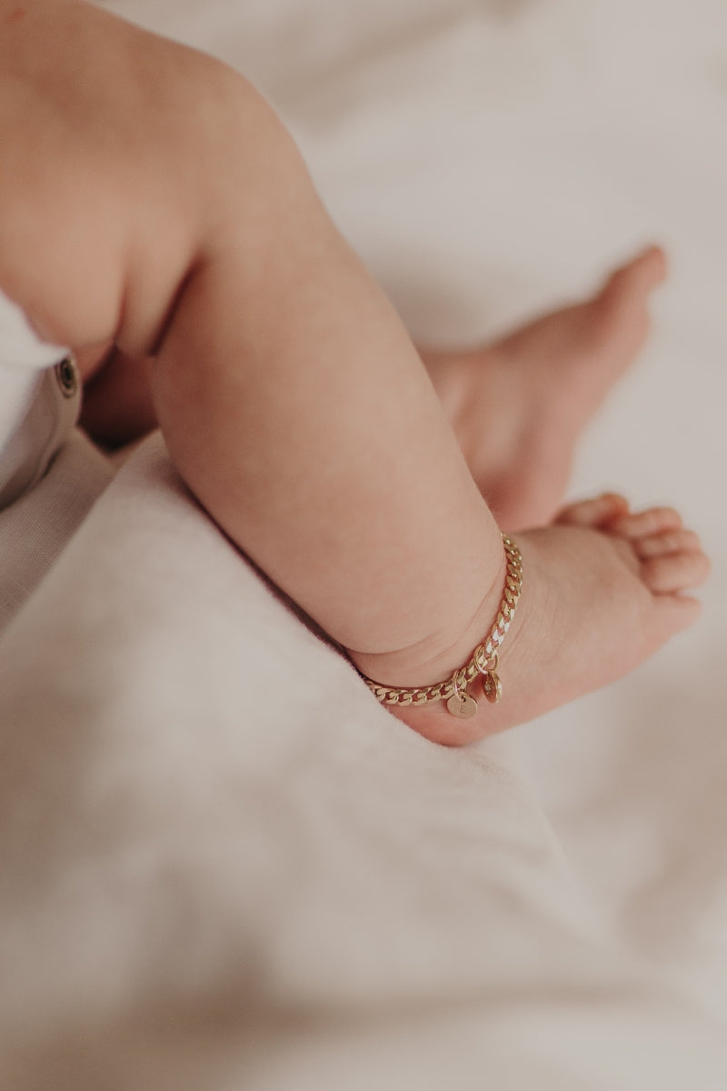 A detailed image of a baby wearing a personalised gold anklet with a daisy charm and engraved initial pendant, crafted as an elegant keepsake piece.