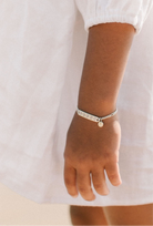 A child wearing a silver Daisy Bracelet by Bluebird Jewellery, featuring five hand-drawn daisies with pink cubic zirconia centres, crafted as a feminine and floral fine jewellery piece along with an initial pendant. 