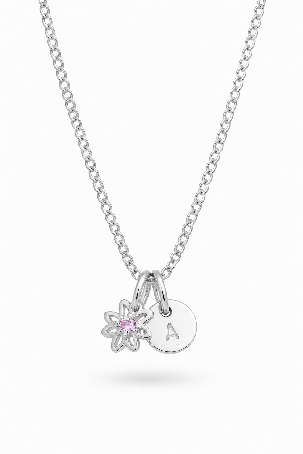 A silver chain necklace with two charms: a small flower charm with a pink gemstone and a round disc charm engraved with the letter 'A', shown on a light gray background.