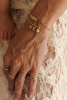 A woman is wearing the Solid Gold Darling Bracelet with the solid Gold Bracelet with solid gold initial pendants and mini sweetheart pendant in solid gold.  The woman also wears three solid Gold Signature Rings.  