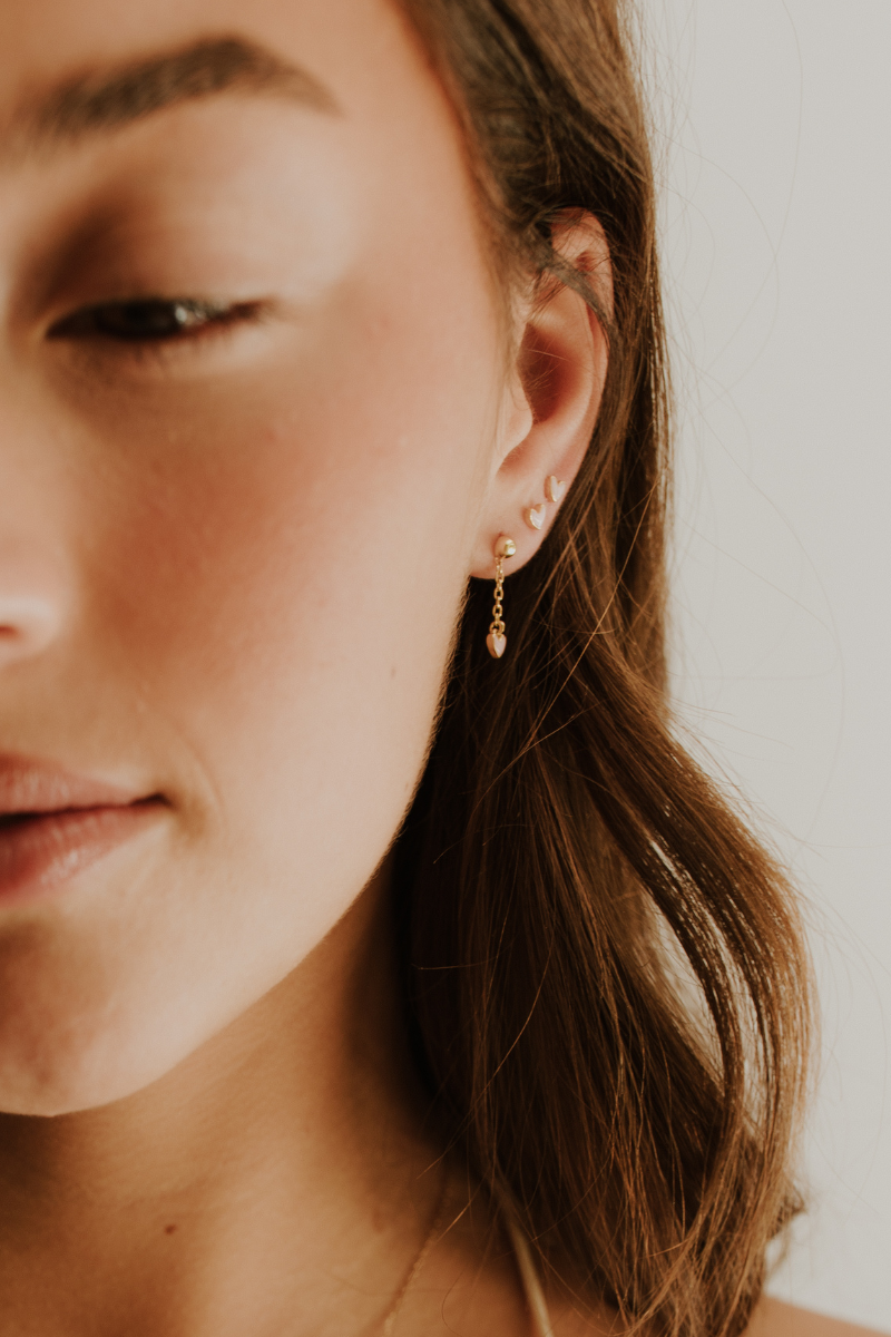 Engraved gold drop earrings with pink heart charm, suitable for everyday wear – model wearing three gold darling earrings 