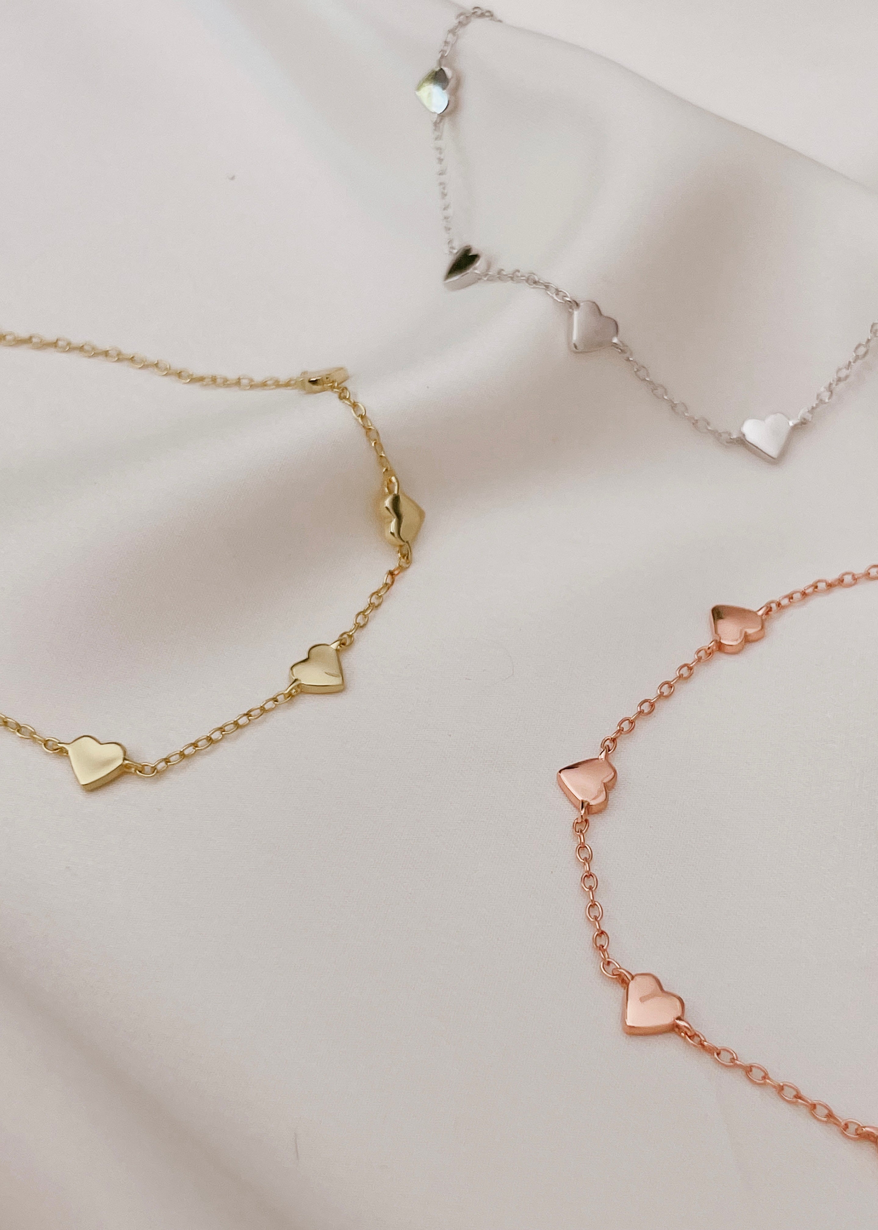 Three Darling Heart Bracelets are featured on a piece of silk in a flat lay