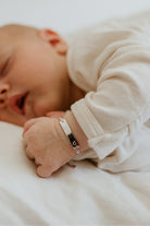 The Darling Bracelet in sterling silver is worn by a baby.  The engravable ID bracelet features a small heart at the end of the bar pendant and has a figaro chain.