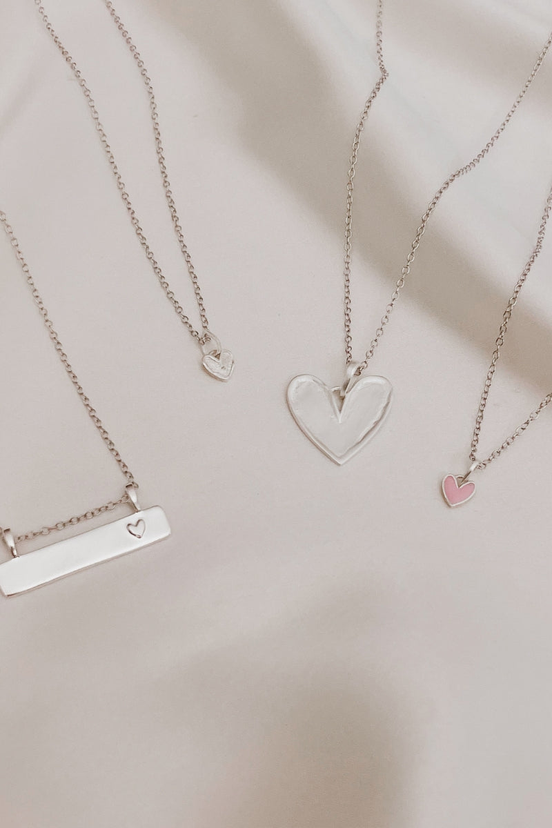 A Darling Bar Necklace, Petite Darling Necklace, Darling Necklace and Pink Petite Darling Necklace are all arranged on silk together.  This shows the various sizes of the heart pendants and the scale of the Bar Pendant next to the Petite and normal sized heart pendants.