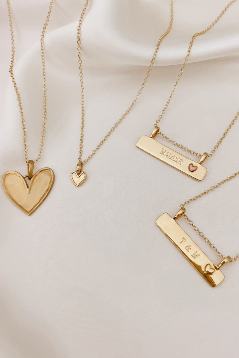 Gold Darling Necklaces are arranged on silk with the Darling Necklace alongside the Petite Darling Necklace, Pink Darling Bar Necklace and Darling Bar Necklace both with personalised engraving on their bar pendants.