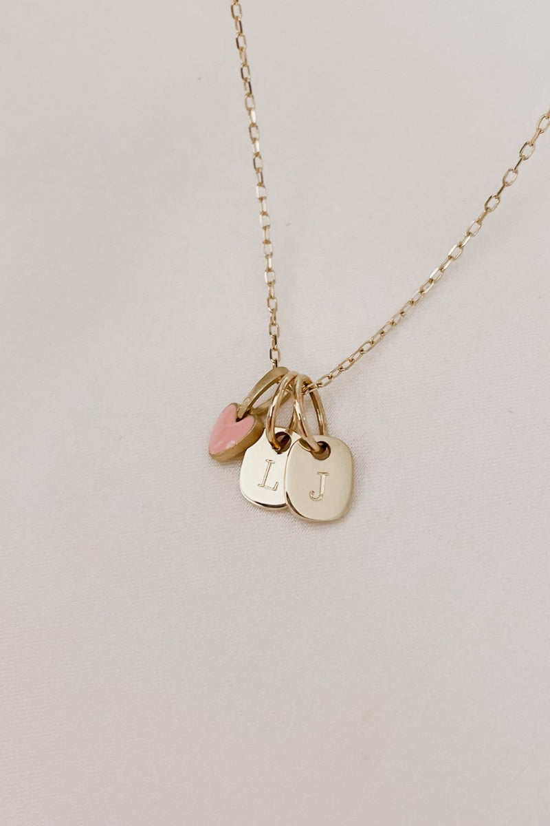 A pink Darling Pendant is on a solid gold chain alongside two mini rectangular pendants also in solid gold
