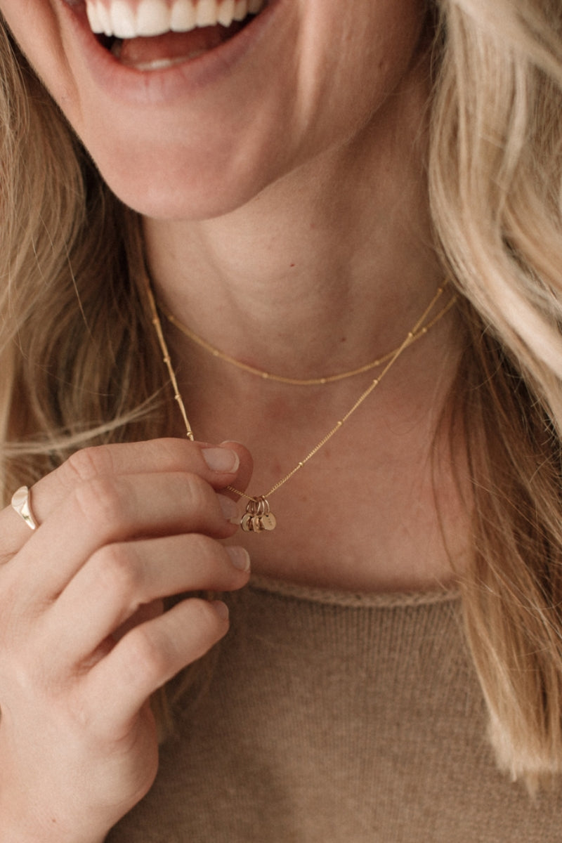 A woman wears the 45cm Gold Petite Personalised Necklace with three solid 9ct initial pendants and is holding out the necklace to show the detailing in the initial pendants.