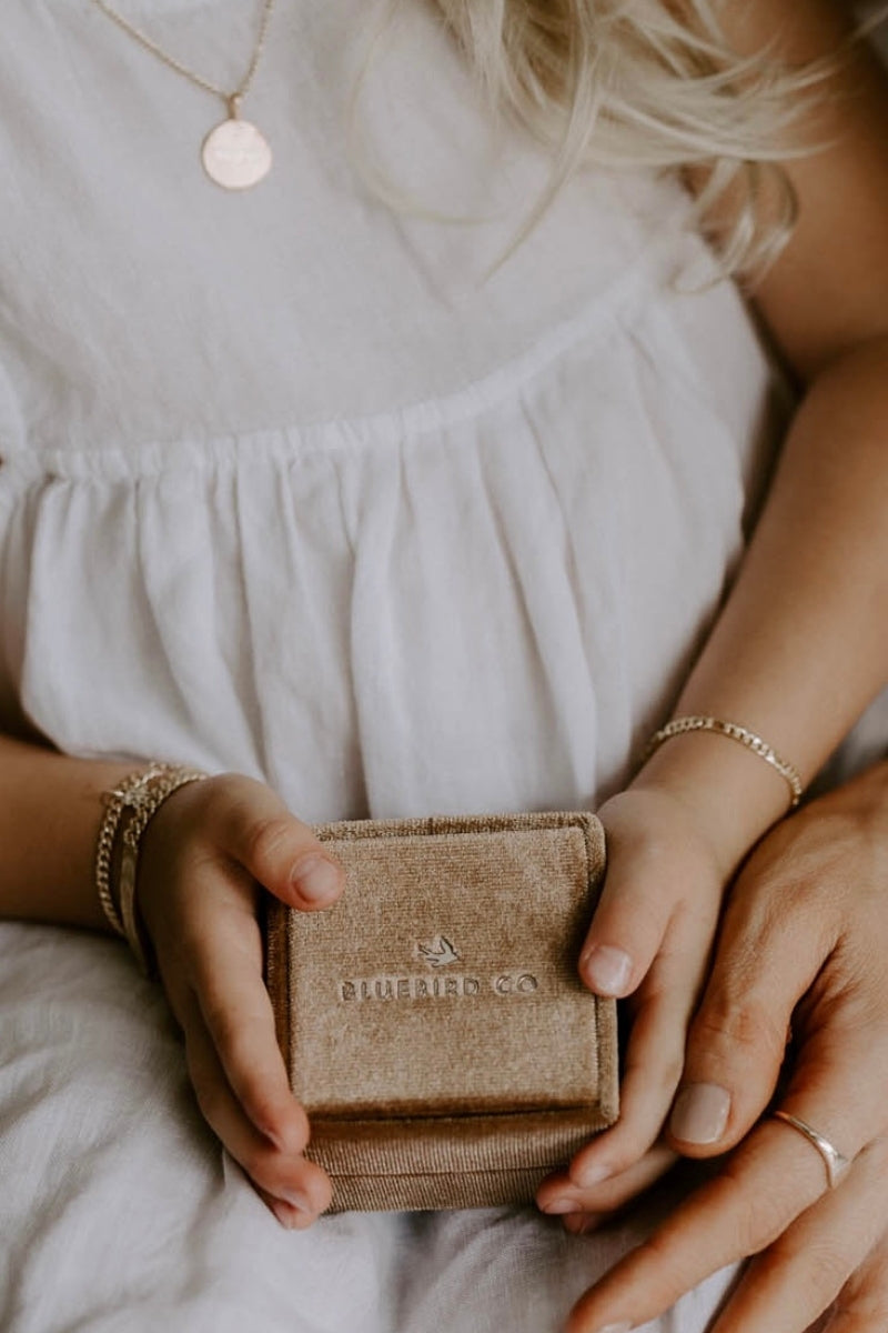 A young girl is holding a velvet gift box with Bluebird Jewellery logo shown close to her Bluebird Co bracelets and personalised necklace.\