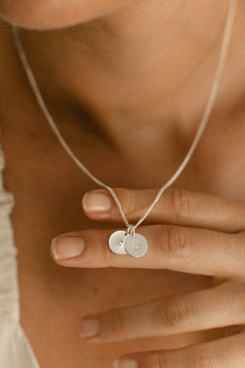 A close up of the round sterling silver initial pendants on the Keeping it Personal necklace.