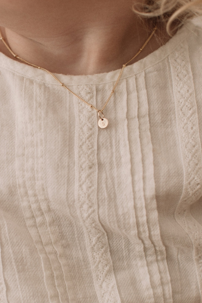 A child is wearing the child length Gold petite Personalised necklace with a solid gold letter pendant that reflects the first letter of her name. 