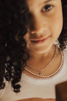 A young girl wears the Freshwater Pearl Necklace with a 35cm Figaro Necklace and Petite Initial Pendant