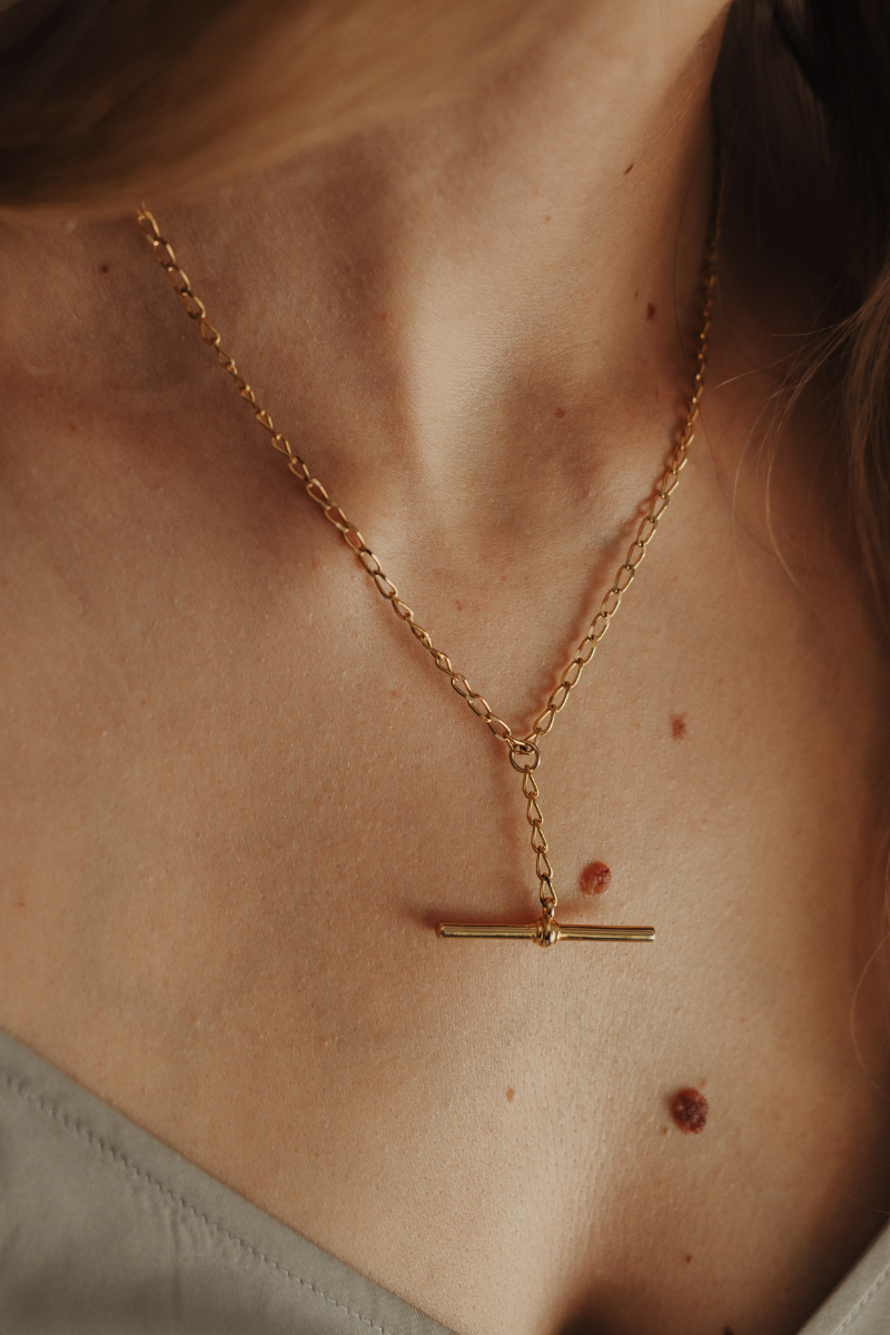 A Gold T-Bar or Fob Necklace on a woman's neck.  A vintage style curb chain woth free moving Bar pendant.