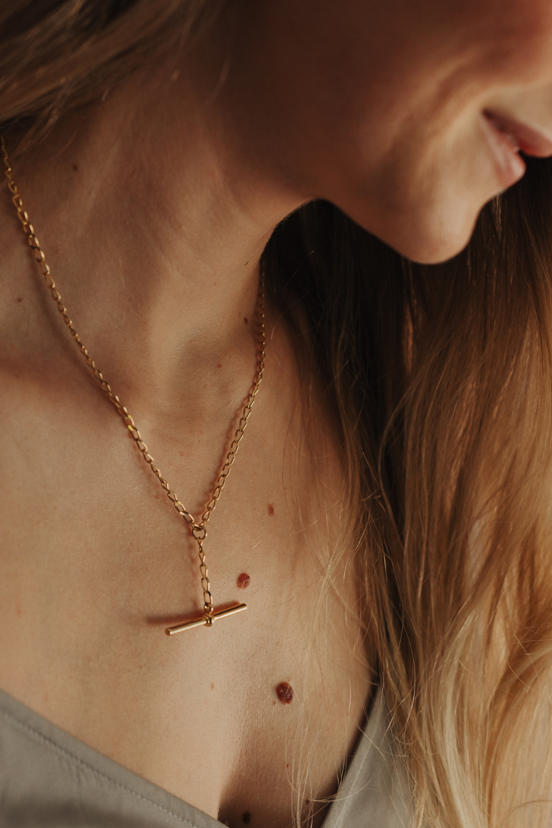 Close-up of a person wearing a gold necklace with a pendant.
