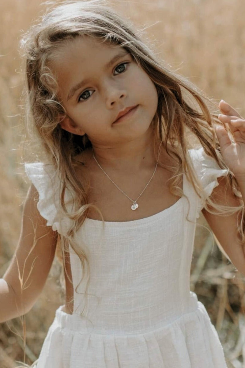 A young girl is standing in a field and is wearing a white dress with a Vintage Pearl necklace that has a personalised initial pendant added to it with her letter pendant.