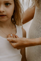 A mother is holding her daughter's Petite Signature Necklace pendant and is looking at the engraving of her initial on the front of the pendant.