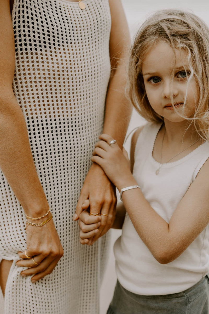 A mother and saughter are standing on the beach wearing matching Signature Bracelets.  The daughter wears the Child Sized personliased bracelet whilst the mother wears a matching bracelet in Gold.