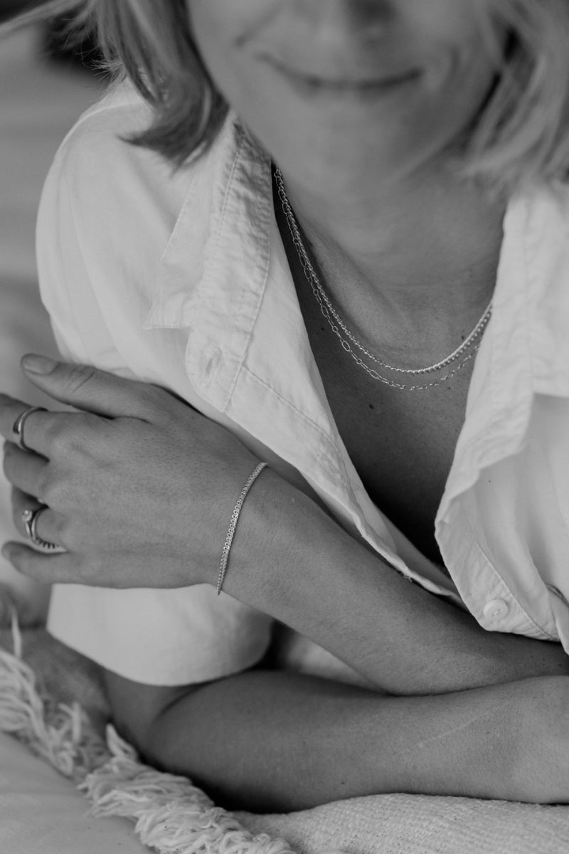 A close-up of a woman wearing silver necklaces including a Lace Chain, complemented by minimalist matching rings, crafted in timeless fine jewellery style.