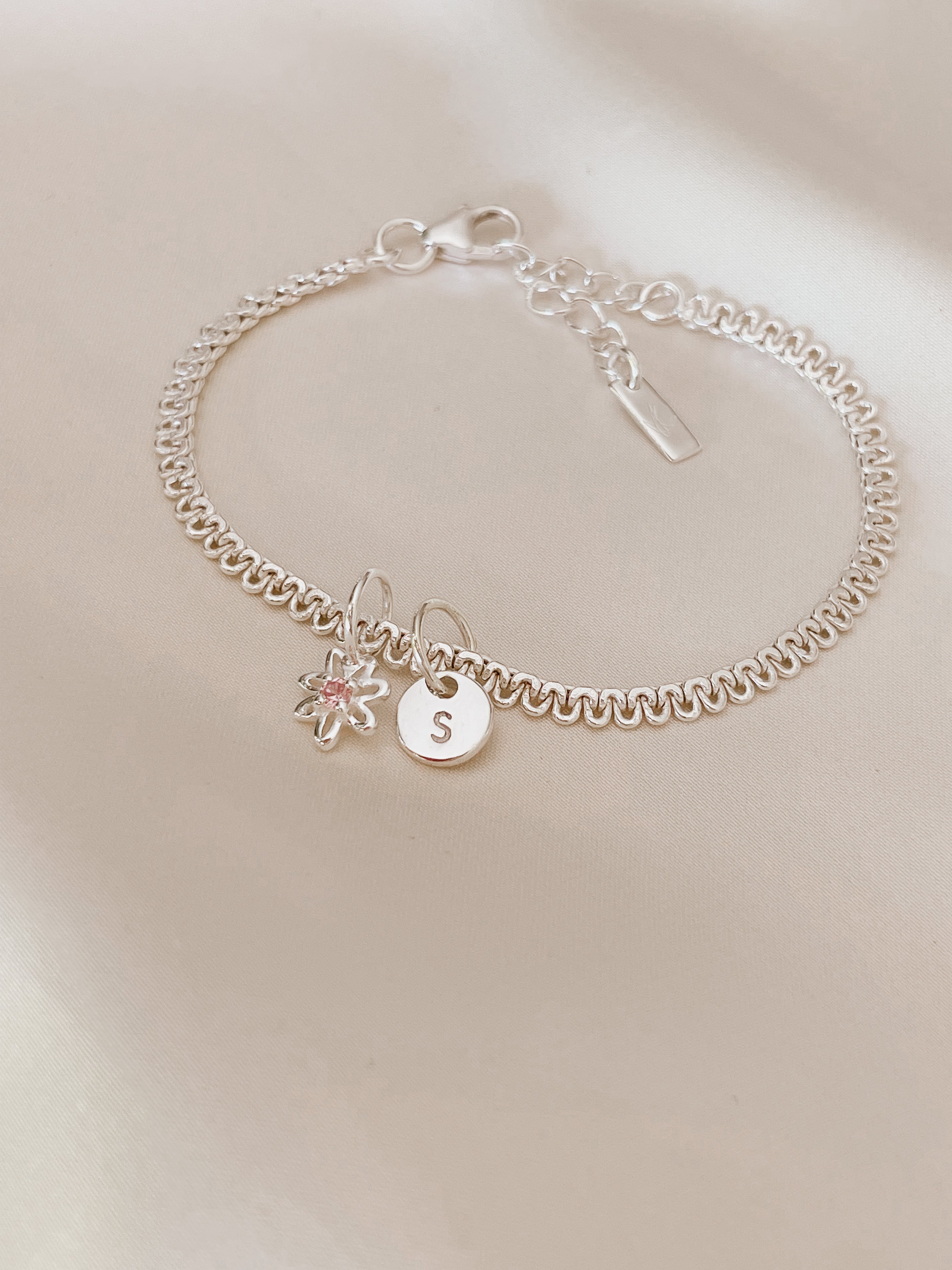 A Baby sized Lace Chain Anklet has a Daisy Pendant and Petite Initial Pendant added to it.